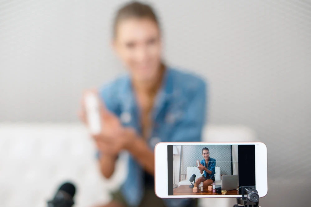 Closeup of a phone recording a woman selling makeup products. She is blurred out in the background.