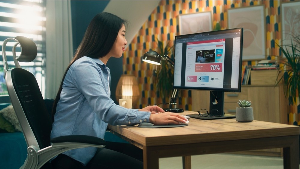 Asian woman sitting at a desk looking at a website.