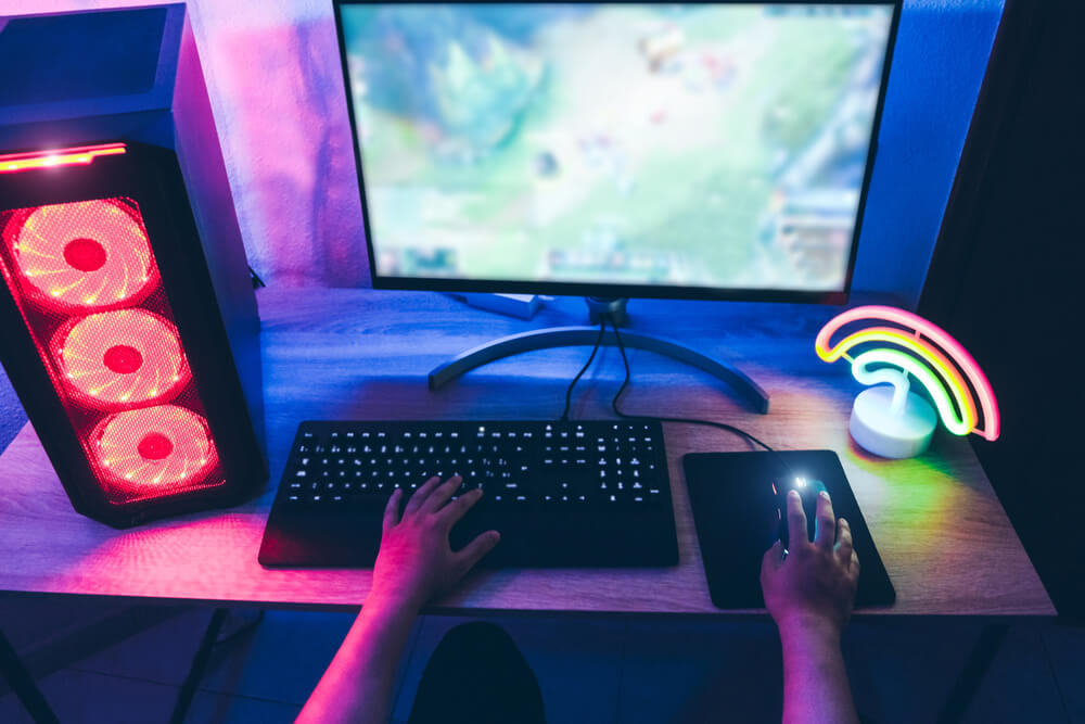 Closeup of a gamer's setup including their keyboard, computer, desktop screen, mouse, and rainbow light. 