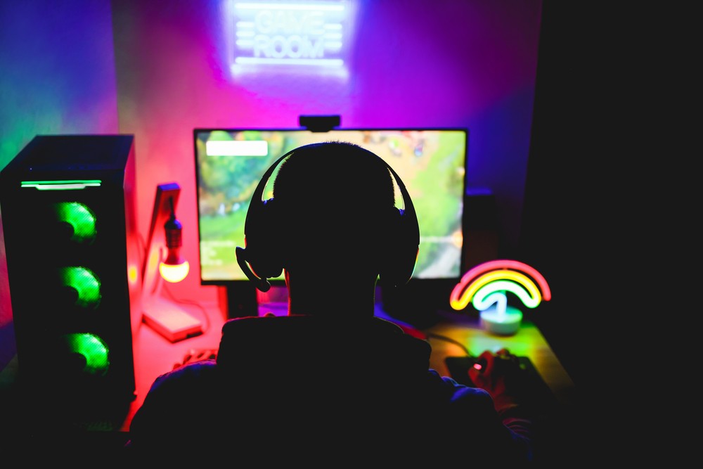 Image of a young man with a gaming setup and rainbow light on his desk playing on his desktop.