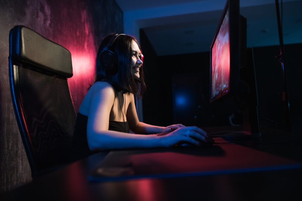 Gamer girl smiling at the camera while playing on her computer.