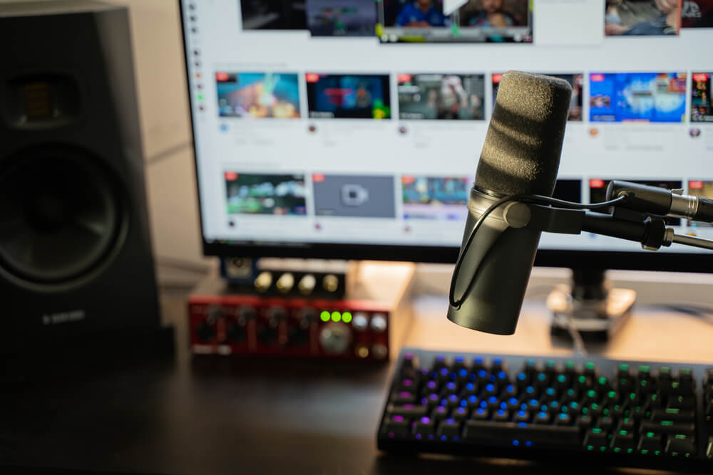 Image of a Twitch setup with a microphone, keyboard, speaker, and video playlist in the background.
