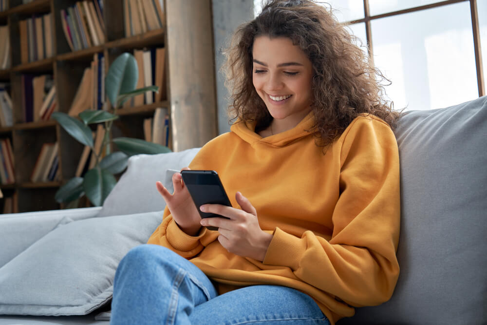 Young woman sitting on a couch shopping on her phone.