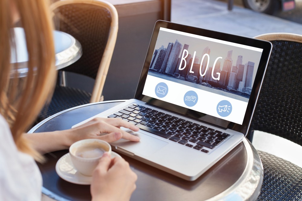 Woman sitting at a small table with coffee cup and her laptop open to a blog.