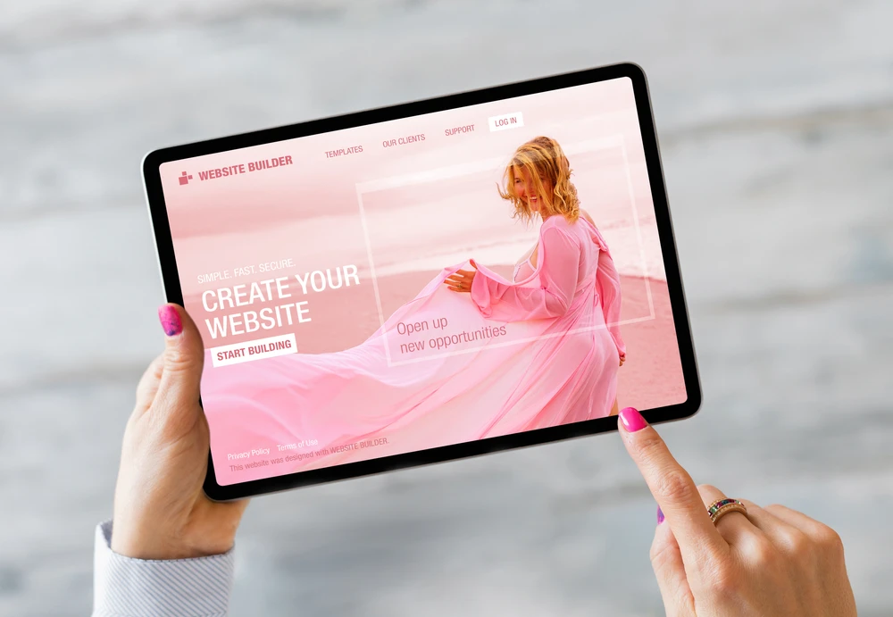 Closeup of hands holding a tablet that is open to a pink website builder.