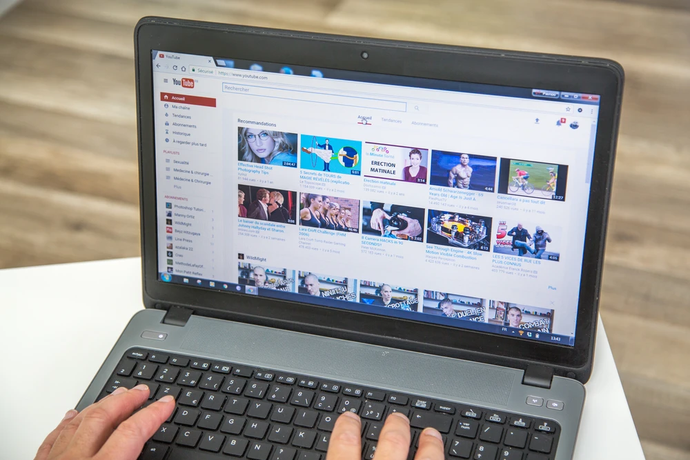 Closeup of hands on a laptop keyboard with the YouTube homepage on the display.
