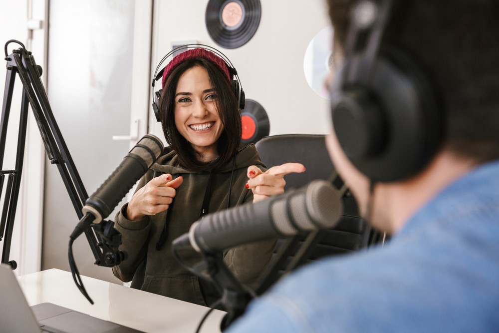 Woman with short hair and a man sitting in front of microphones making a podcast.