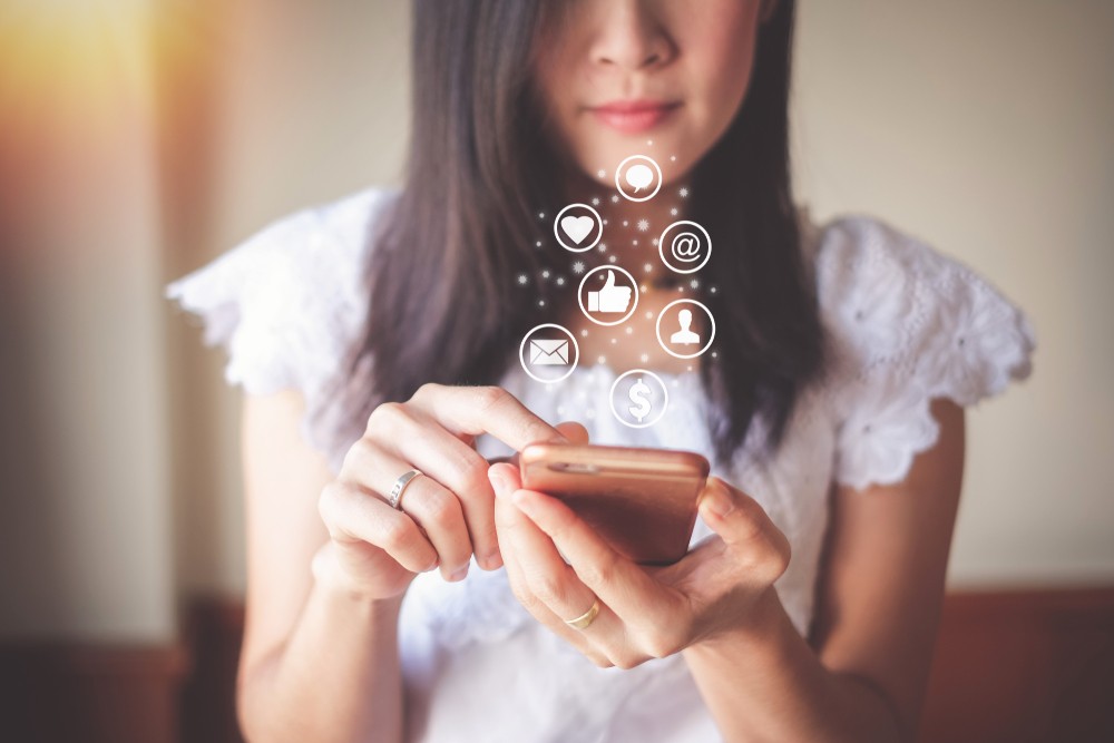 Woman wearing a white top holding her phone and checking social media notifications.