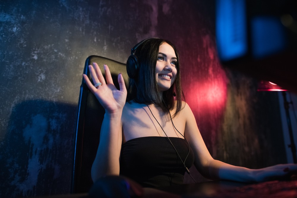 Young woman with short black hair waving at the camera while gaming.
