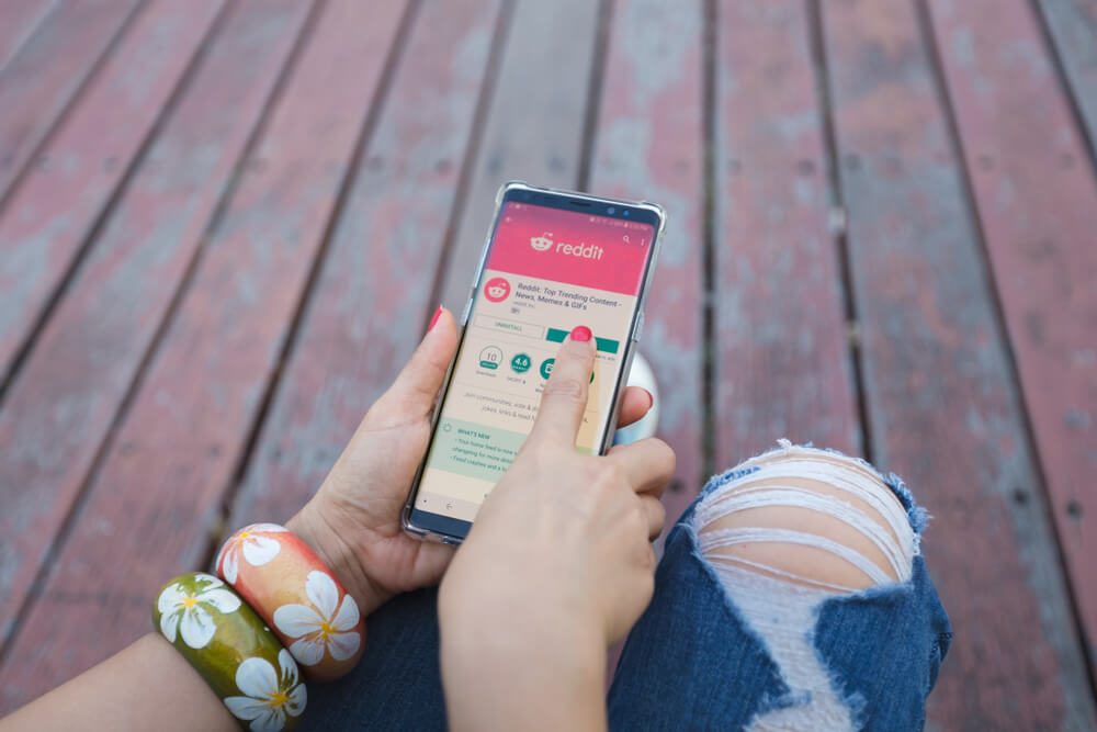 Closeup of woman's hands holding a phone with the reddit app open.
